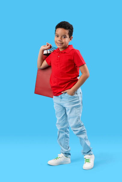 Kis afro-amerikai fiú, kék hátterű bevásárlószatyrokkal. Gyermeknapi ünnepség - Fotó, kép