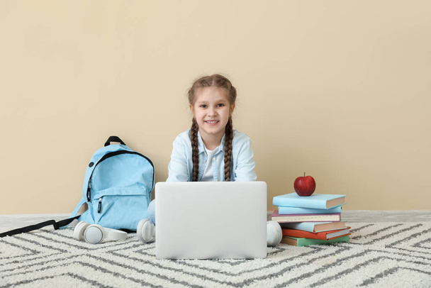 Little girl studying with laptop near beige wall. Children's Day celebration - Fotoğraf, Görsel