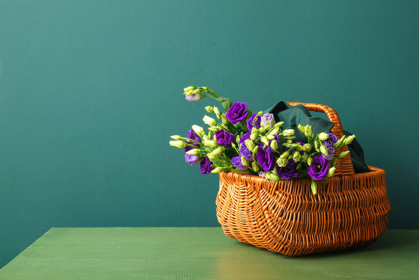 Basket with eustoma flowers on table near blue wall - Фото, зображення