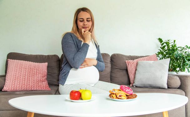A pregnant woman eats a sweet donut. Selective focus. Food. - Photo, Image