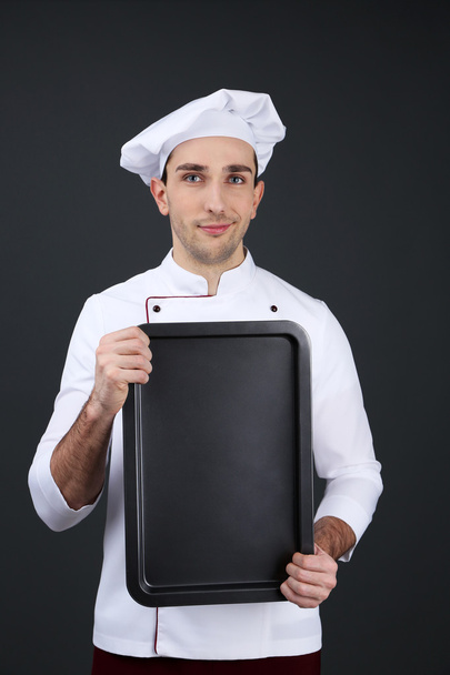 Portrait of chef with oven pan in hands on dark background - Fotó, kép