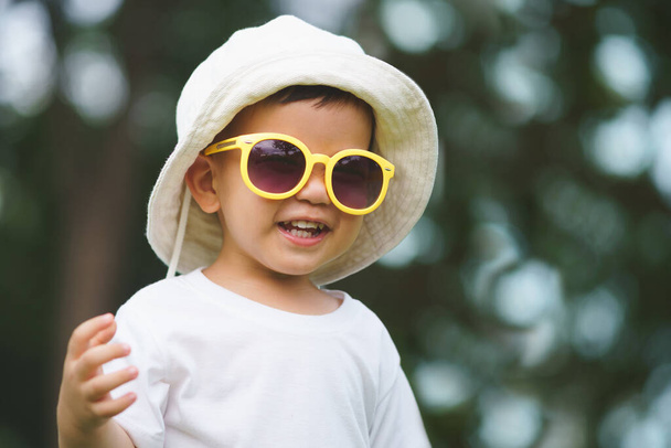 Portrait of Happy Asian Chinese little child boy wearing hat and yellow sunglasses smiling outdoor - 写真・画像