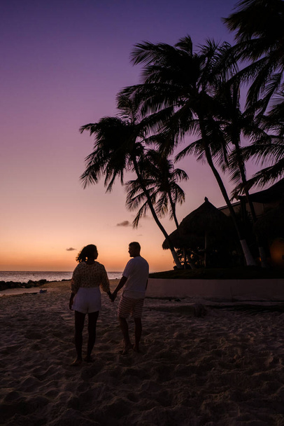 Un par de hombres y mujeres están en la playa observando la puesta de sol durante las vacaciones en Aruba Island Caribbean. pareja madura en la playa  - Foto, Imagen