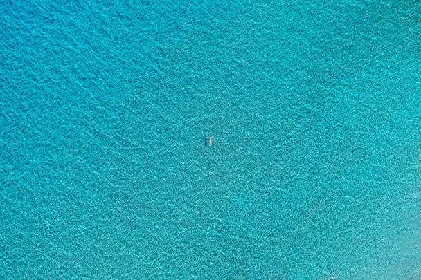 Aerial view of a woman floating on a crystal clear turquoise sea water. Top down view of a swimming woman in clear azure water. Transparent water in Ionian sea, Greece. - Foto, afbeelding