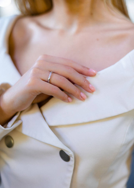 Tyylikäs tyttö pitää kaulus hänen valkoinen takki, esittelee kaunis ja arvokas timantti koruja putiikki. Nainen seisoo jalokivikaupassa sinistä taustaa vasten keskittyen sormukseen. - Valokuva, kuva