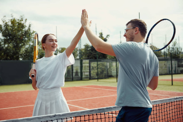 Yakışıklı adam ve güzel kadın beşlik çakıyor ve gülümsüyor. Arkadaşlarla aktif spor oyunu. Tenis oyuncusu iş başında. Tenis maçı. Aktif boş zaman oyunu. Eğlence için hafta sonu etkinliği - Fotoğraf, Görsel
