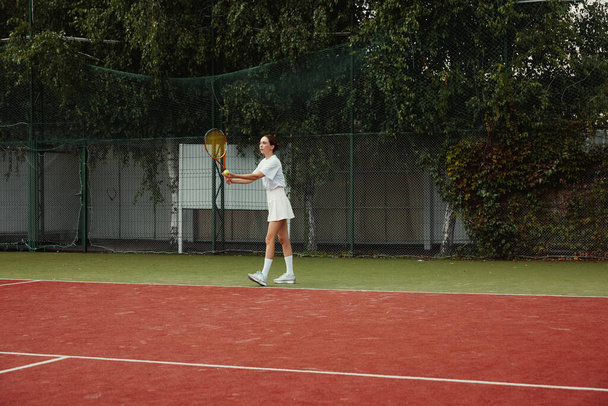 白い衣装のテニス選手が試合でボールを提供しています。若いです女の子プレイテニスでコート屋外. - 写真・画像