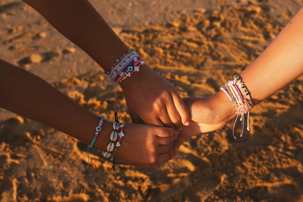 Дружба жінок. Обкладинка Three Friends Holding Hands Wears Cute Bracelets And Wristbands Over Sand Hanging At Beach Together, Enjoying Summer Day At Seaside Outdoor. Шалений постріл - Фото, зображення