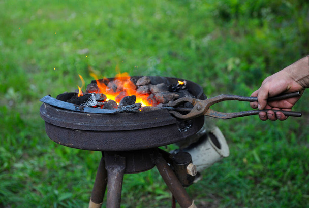 Forgeron main tenant des pinces avec une billette en métal dans une forge ardente rougeoyant - Photo, image