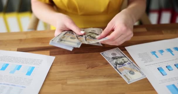 Zaměstnankyně počítá peníze v hotovosti, když sedí u stolu s dokumenty ve firmě. Účetní vypočítává mzdy pracovníků na zpomaleném pracovišti - Záběry, video