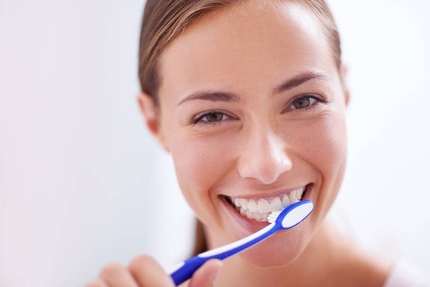 Young woman, portrait and brushing teeth in bathroom with smile, health or self care for hygiene, grooming and routine. Girl, toothbrush and happiness for cleaning, healthy mouth and start morning. - Photo, Image