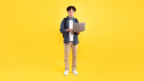 Дистанційне навчання. Захоплюючий студент, який використовує Laptop Computer Engaging In Online Education Standing Over Yellow Studio Background. Internet Technology та E-Learning Offers. Панорама - Фото, зображення