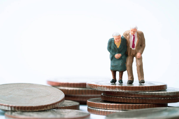 Pár Senior Pensioners miniaturní postava stojící na vrcholu mince stohování pro finanční plánování bohatství, peníze úspory a životní pojištění důchodového konceptu.  - Fotografie, Obrázek