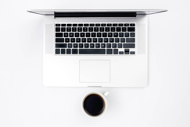 Fondo blanco minimalista con un ordenador portátil y una taza de café negro, vista superior. - Foto, Imagen