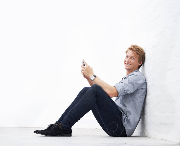 Muž, telefon a podlaha s prostorem po stěně v portrétu, komunikace nebo textové aplikace s úsměvem. Mladý podnikatel, podnikatel a štěstí sedí s chytrým telefonem v maketu pro sociální média chat. - Fotografie, Obrázek