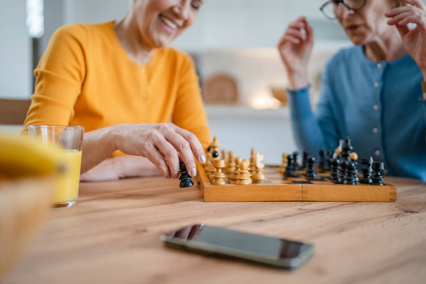 two senior mature women caucasian female woman friends or sisters play leisure chess board game at home have fun spend time together at home bright photo copy space - 写真・画像