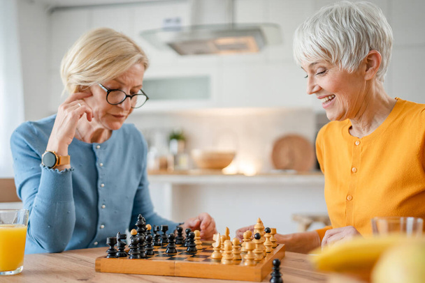 zwei ältere reife Frauen kaukasische Freundinnen oder Schwestern spielen Freizeitschach Brettspiel zu Hause haben Spaß verbringen Zeit zusammen zu Hause helle Fotokopierraum - Foto, Bild