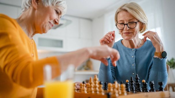 two senior mature women caucasian female woman friends or sisters play leisure chess board game at home have fun spend time together at home bright photo copy space - Photo, Image