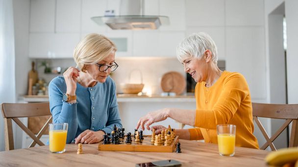 二人のシニア熟女白人女性の友人や姉妹遊びレジャーチェスボードゲーム自宅で楽しい時間を過ごしています一緒に家で明るい写真のコピースペース - 写真・画像