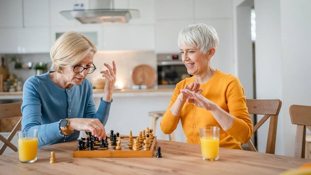twee senior volwassen vrouwen Kaukasische vrouw vrienden of zussen spelen vrijetijdsschaken bordspel thuis veel plezier breng tijd samen thuis heldere foto kopieerruimte - Foto, afbeelding
