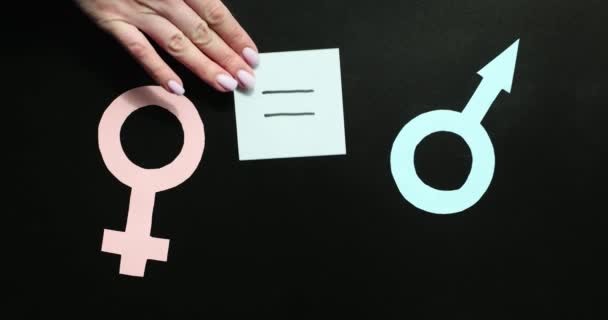 Mano de mujer poniendo signo de ecuación entre símbolos femeninos y masculinos sobre fondo negro. Igualdad de género entre hombres y mujeres en la sociedad moderna - Imágenes, Vídeo
