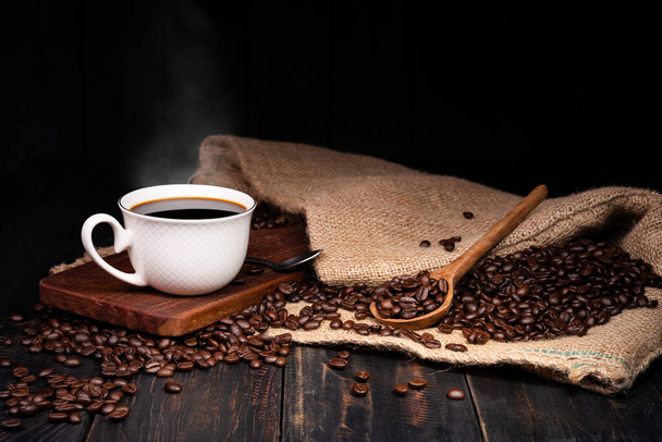 Vers gebrouwen koffie. Koffiebeker of mok op een zwarte houten tafel met gebrande koffiebonen. Espresso mocha cappuccino barista op donkere achtergrond - Foto, afbeelding
