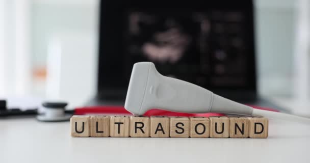 Word Ultrasound gemaakt van houten kubussen met moderne ultrasone apparatuur op de top. Medische transducer sonde op tafel tegen scherm in kliniek - Video