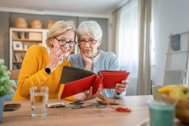Старші зрілі жінки друзі або сестри дивляться сімейний фотоальбом дві кавказькі жінки сидять вдома щаслива посмішка, поки відкликають спогади реальні люди копіюють простір
 - Фото, зображення