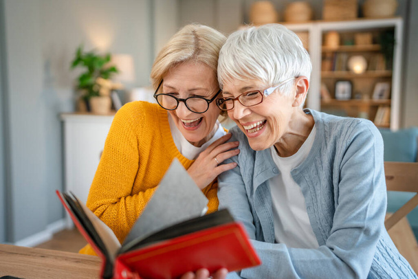 Senior érett nők barátok vagy nővérek keres családi fotók album két kaukázusi nő ül otthon boldog mosoly, miközben visszavonja emlékek valós emberek másolja tér - Fotó, kép