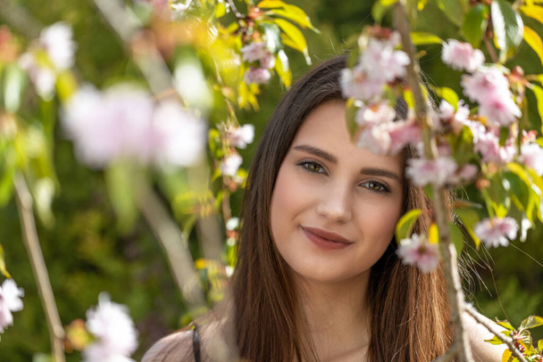 Cool brunette girl posing behind sprig of cherry blossoms.  Horizontally.  - Fotoğraf, Görsel
