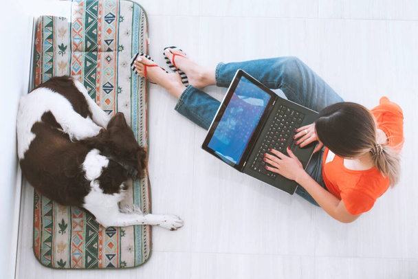 Young woman lying on the floor with her dog and working on a laptop - Foto, imagen