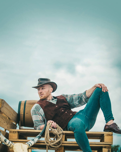 Cowboy farmer man in country side wearing western cowboy hat. American Male model in countryside on farm. Men retro fashion, vintage vogue, brutal male model - Φωτογραφία, εικόνα