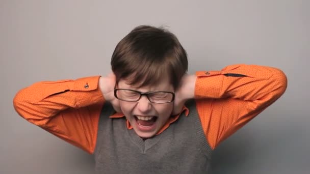 genç çocuk onun elleri yüksek sesli sağlam gri arka plan üzerine gözlük ile kulakları kapalı - Video, Çekim