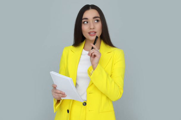Young female intern with pen and notebook on grey background - Photo, Image