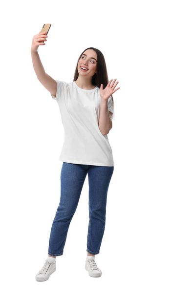 Smiling young woman taking selfie with smartphone on white background - Foto, afbeelding
