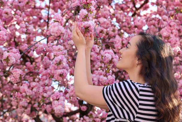 Beautiful woman near blossoming sakura tree on spring day - Фото, зображення
