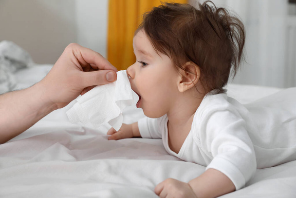 Father taking care of little baby suffering from runny nose in bed, closeup - Photo, image