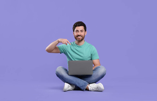 Happy man with laptop on purple background - Фото, зображення