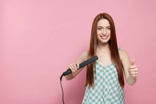 Beautiful woman using hair iron and showing thumbs up on pink background, space for text - Photo, image