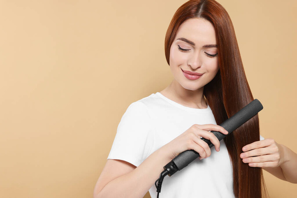 Beautiful woman using hair iron on beige background, space for text - Fotografie, Obrázek