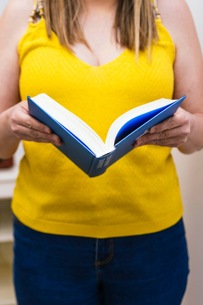 Крупним планом руки жінки, одягнені в жовтий отвір книги
. - Фото, зображення