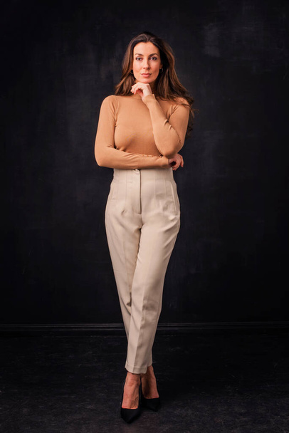 Full length of an attractive mid aged woman wearing sweater and pants and standing at isolated dark background.  - 写真・画像