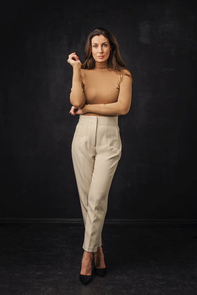 Full length of an attractive mid aged woman wearing sweater and pants and standing at isolated dark background.  - Foto, immagini