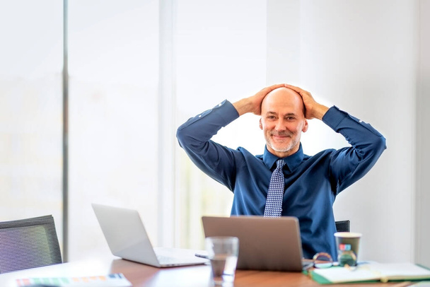 Shot of mid aged businessman sitting in a modern office and using laptops for work. Professional male wearing shirt and tie. Hand on head.  - Valokuva, kuva