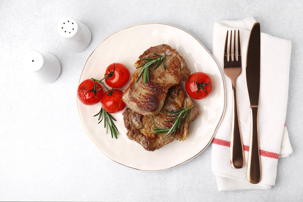 Delicious fried meat with rosemary and tomatoes served on light grey table, flat lay - 写真・画像