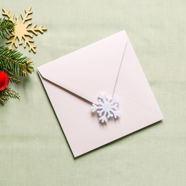 Christmas still festive life. Blank invitation mockup, envelope on textile background. Fir branches, wooden snowflake, red christmas ball on the table. Copy space, top view. - Foto, Imagen
