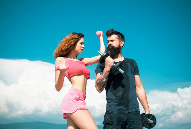 Fit couple doing exercising outdoors with dumbbell. Sportive woman and man, team. Sport, dumbbell and fitness, couple sports. Sporty sexy couple showing workout wiht dumbbells. Sports fitness girl - Foto, imagen