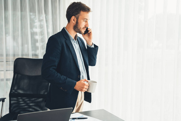 Hardworking businessman stand confidently in modern office making persuasive sales call to client. Office worker talking on the phone coordinate and manage business work with colleagues. Entity - Φωτογραφία, εικόνα