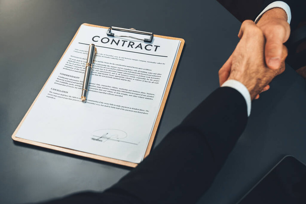 Focus business contract paper with blur background of handshake after successfully close business deal, sealing partnership agreement. Legal document and handshaking as formal agreement. Fervent - Foto, afbeelding