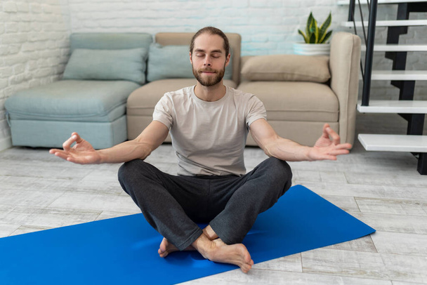 Mindful man meditating at home, peaceful calm guy practicing yoga in lotus pose holding hands in mudra. - Foto, Imagem